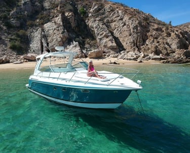A luxury motorboat anchored in turquoise waters near a rocky coastline and sandy beach.