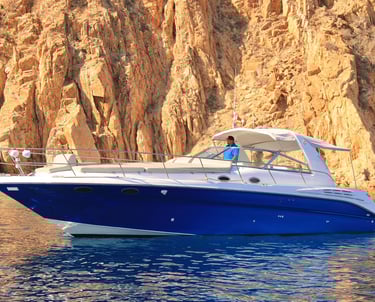 A luxury blue and white powerboat yacht cruising past rugged golden desert cliffs on the ocean.