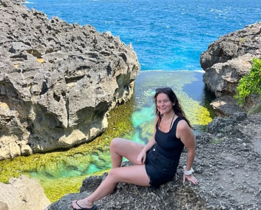 A woman sits on volcanic rocks by the turquoise waters of Angel's Billabong in Nusa Penida, Bali.