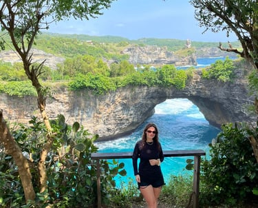 A woman stands before the scenic Broken Beach natural bridge arch in Nusa Penida, Bali.