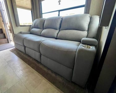 Modern gray leather power reclining sofa with integrated cup holders inside a motorhome living area.