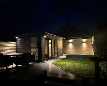 Modern garden room and patio with warm outdoor lighting and garden furniture at night.