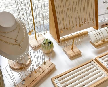 Collares, anillos y pulseras de oro colgando en un exhibidor de soportes de joyería de madera.