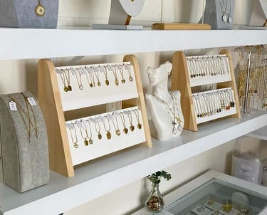 Elegante exhibición boutique con collares de oro y joyas de perlas en estantes y bustos blancos.