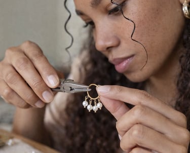 Joyero utilizando alicates para elaborar aretes de oro y perlas hechos a mano en su lugar de trabajo