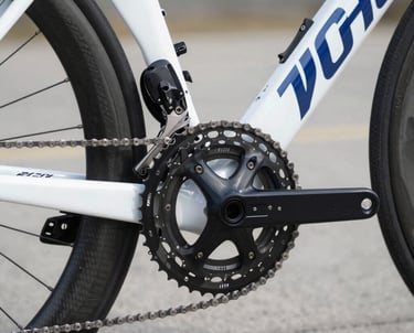 A close-up shot of professional cycling gears, chain, and a sleek carbon fiber bike frame. Clean white and deep blue colors, technical detail, modern and highly professional sports photography, bright lighting with subtle shadows, crisp focus.