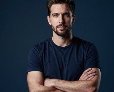 Professional portrait of a male cinematographer in a studio setting. Dramatic lighting, deep blue tones in the background, confident and artistic posture.