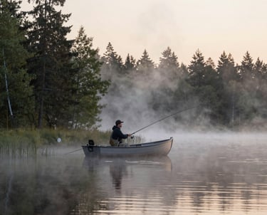 A serene Finnish lake at dawn with a person fishing from a small boat surrounded by misty forest.