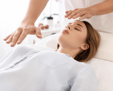 Sesión de Reiki en una camilla de terapeuta, vemos a una mujer joven recibiendo energía reiki del terapeuta, en parte superio