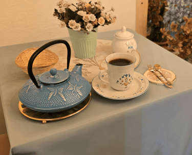 Vintage blue cast iron teapot and floral ceramic coffee cup on a table with flowers.