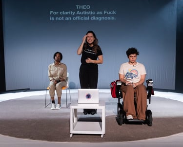 Three figures on a stage, Evlyne seated, Anna stood, and Theo seated