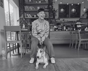 Mujer riendo sentada junto a su Bull Terrier Inglés en una cafetería moderna.