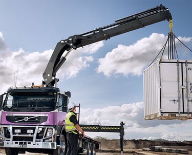 A knuckle boom crane with RC lifting a container onto a truck.