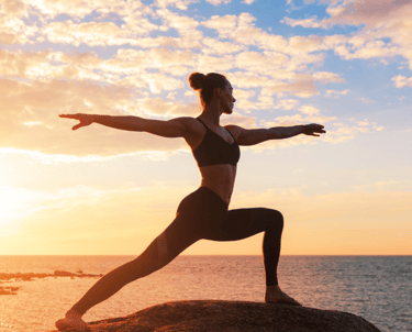 Woman yoga pose beside the ocean at sunset