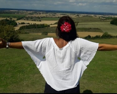 An image of the back of Sheila Cristina on the top of a hill. In front of her is a beautiful view of many fields in England.