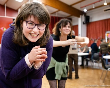 a woman in glasses and a purple sweater is smiling and holding a wii game controller