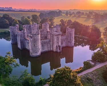 Bodium Castle at sunrise. a moat and trees.