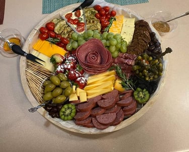 Gourmet charcuterie board with a salami rose, assorted cheeses, crackers, grapes, and olives.