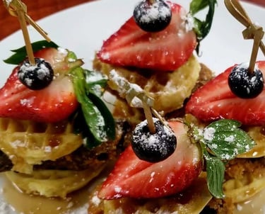 Mini chicken and waffle sliders topped with strawberries, blueberries, and powdered sugar.