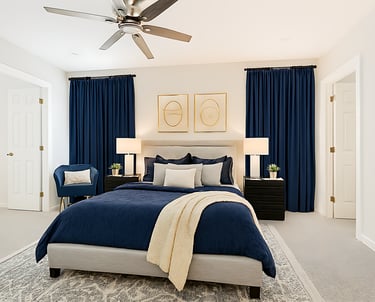 Modern bedroom interior with a blue comforter, navy curtains, and gold wall art frames.