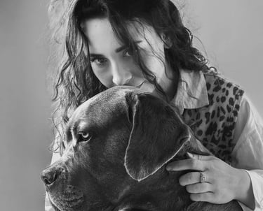 Black and white portrait of a woman with curly hair hugging a large Cane Corso dog.