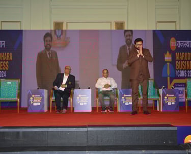 Speaker addressing an audience at a business event with panelists on stage.
