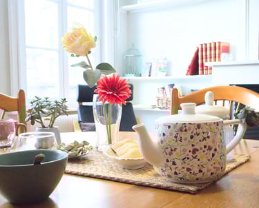 Table conviviale avec théière, fleurs et vaisselle dans logement meublé pour professionnels.