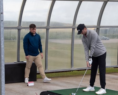 A golf coach in Aberdeen gives a full swing lesson at the driving range, using a launch monitor to evaluate student's swing