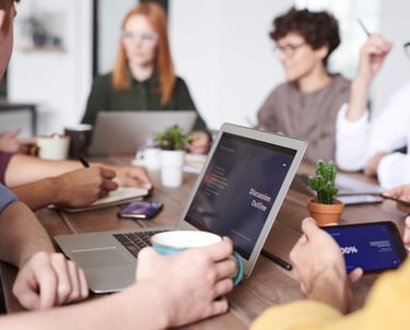 a group of people sitting around a table with laptops