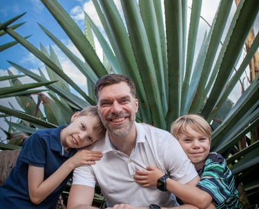 Father sits with his two sons in front of dramatic agave plants in Madeira botanical garden, lifestyle family portrait.