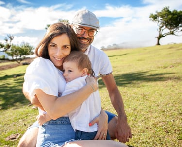 Close-up of toddler holding each parent's hand, smile on face, bright laurel forest background, intimacy and connection.