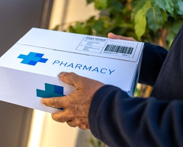 Person holding a white delivery box labeled “Pharmacy” with a medical cross symbol, representing pre