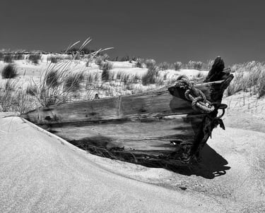A vintage boat rests on the sandy shore in a black and white photograph