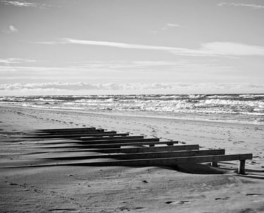 A black and white photo depicting a peaceful beach with wooden benches