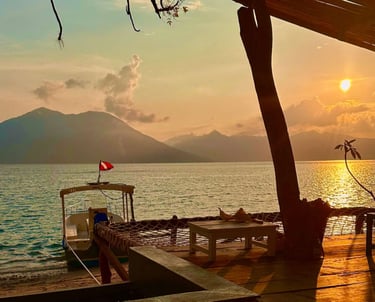 Tropical beach sunset at a resort with a docked boat and mountain views over the calm ocean.