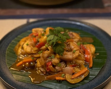 Spicy Thai shrimp stir fry with vegetables and cilantro on a banana leaf plate.