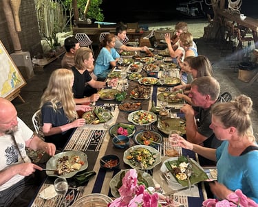 A group of friends enjoying a communal dinner of local island cuisine at a tropical beach resort at night.