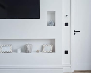 Minimal, white living room with a tv and small alcoves containing ornaments and picture frames