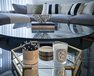 elegant, mirrored, circular coffee table with a tray, books and candles, set against a sofa backdrop