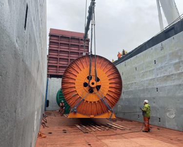 Industrial reel being lifted onto a cargo ship with workers and cranes