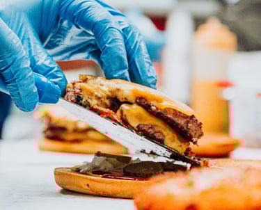 Montaje de hamburguesa doble con cheddar en cocina de Flipa, preparado con guantes y espátula