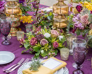 beautiful wedding tablescape with purple linens and bold colored flowers, candles and purple glasses