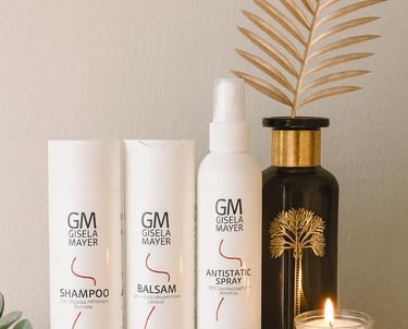 Produits capillaires Gisela Mayer alignés sur une étagère avec une bougie et une décoration dorée.