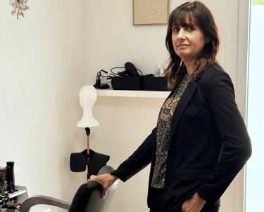 Femme debout à côté d’un fauteuil dans une pièce lumineuse, décorée de façon simple et élégante.