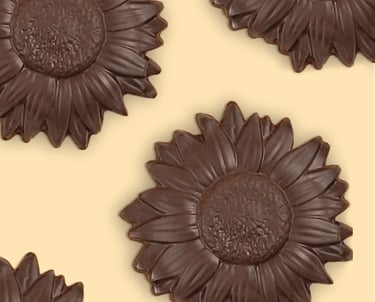 Dark chocolate sunflower shaped candies arranged on a pale yellow background.