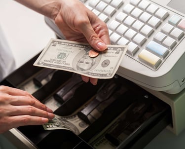 a person holding a dollar bill in front of a cash register