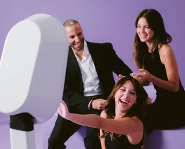 Friends smiling and laughing while using a modern digital photo booth at a purple themed event.