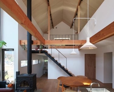 Modern open-plan living area featuring vaulted ceilings, exposed wood beams, and a wood-burning stove.
