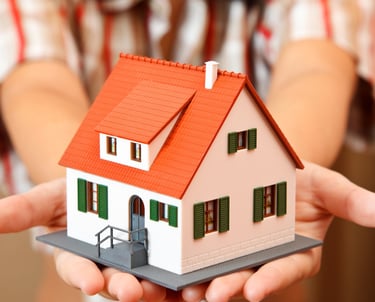 a woman holding a small model of a house