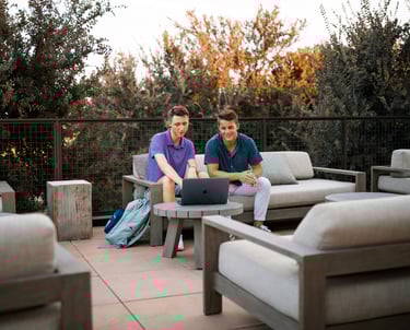 two men sitting on a patio with laptops